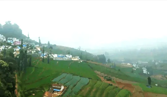 Green fields and hillside homes beneath mist-covered mountains